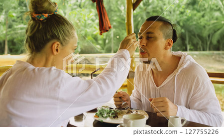 Man and woman eat and drink tasty beverages spending time in traditional local floating cafe on water. Loving happy couple having breakfast outdoors 127755226