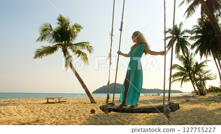 Sexy woman spends her vacation at the seaside. The girl is swinging on a swing. Concept happy holidays, joy, lightness, fresh air, cleanliness and health. 127755227