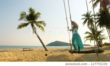 Seductive woman swinging on a swing on a tropical beach, on shores of the turquoise sea. Concept travel, walks, rest in sea, tropical resort coastline relaxation traveling tourism summer holidays. 127755230