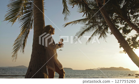 Woman drinking pineapple cocktail Pina Colada near palm tree, in white shirt, sunglasses. Concept rest tropical sea traveling tourism summer holidays Woman drinking pineapple cocktail Pina Colada near palm tree, in white shirt, sunglasses. Concept rest tropical sea traveling tourism summer holidays 127755260