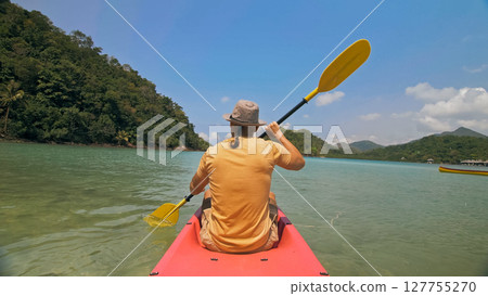 Man with sunglasses and hat rows pink plastic canoe along sea ag 127755270