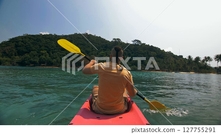 Man with sunglasses and hat rows pink plastic canoe along sea ag 127755291
