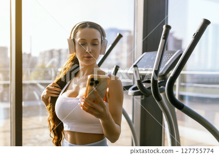 Portrait of young sportswoman with smartphone listening to music in gym. 127755774