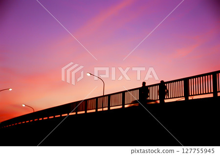 Sunset sky and silhouettes of people walking on a footbridge 127755945