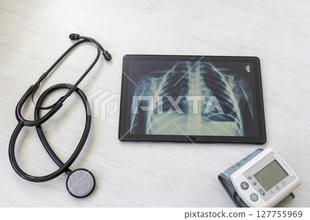 Table with phonendoscope, sphygmomanometer and a X ray image of the lungs with pneumonia on the tablet Table with phonendoscope, sphygmomanometer and a X ray image of the lungs with pneumonia on the tablet 127755969