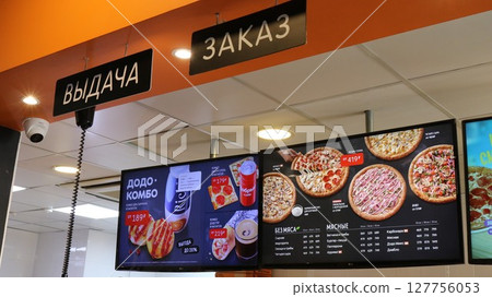 Maykop, Republic of Adygea, Russian Federation - 06.26.2025: Electronic signboard of the Dodo Pizza pizzeria in the cafeteria above the place where orders are issued with a menu in Russian Maykop, Republic of Adygea, Russian Federation - 06.26.2025: Electronic signboard of the Dodo Pizza pizzeria in the cafeteria above the place where orders are issued with a menu in Russian 127756053