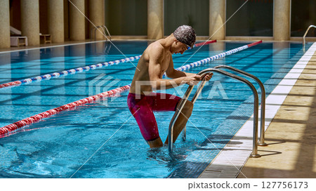 Male swimmer climbing out of indoor pool wearing swim cap and goggles 127756173
