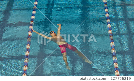 Man floating on back in swimming pool lane with blue water and reflections 127756219