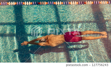 Athlete swimming freestyle in outdoor pool under sunlight with shadow and ripple effects Athlete swimming freestyle in outdoor pool under sunlight with shadow and ripple effects 127756243