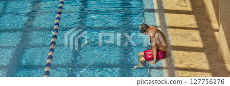 Man in swimwear sitting on pool edge dipping toes in clear blue water Man in swimwear sitting on pool edge dipping toes in clear blue water 127756276