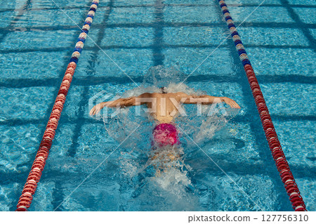 Competitive swimmer doing butterfly stroke in clear blue swimming pool lanes Competitive swimmer doing butterfly stroke in clear blue swimming pool lanes 127756310