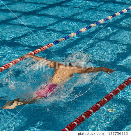 Swimmer executing butterfly stroke in outdoor swimming pool lane during sunny day practice 127756313