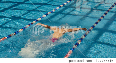 Competitive swimmer practicing butterfly stroke in clear blue swimming pool lanes Competitive swimmer practicing butterfly stroke in clear blue swimming pool lanes 127756316