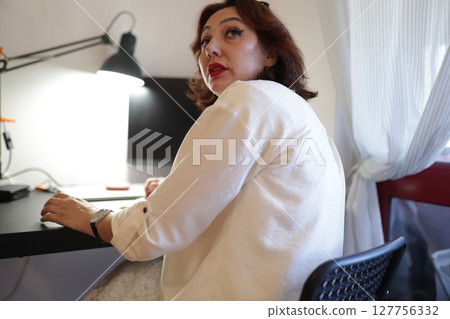 Woman working from home office turning around looking backwards Woman working from home office turning around looking backwards 127756332