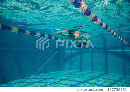 Underwater swimmer gliding beneath surface in pool lane marked with blue and red float dividers Underwater swimmer gliding beneath surface in pool lane marked with blue and red float dividers 127756361