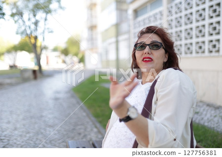 Businesswoman gesturing while sitting on bench in city park 127756381