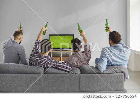 Back view of young men sitting on couch, watching soccer match and drinking beer Back view of young men sitting on couch, watching soccer match and drinking beer 127756554