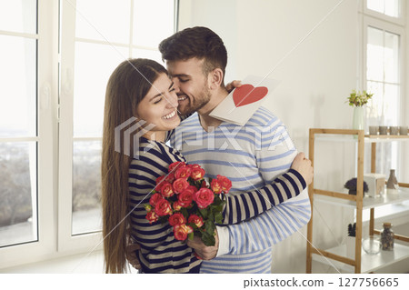 Valentine's day. The guy gives a Valentine with a red heart to a girl standing at the window in the room 127756665
