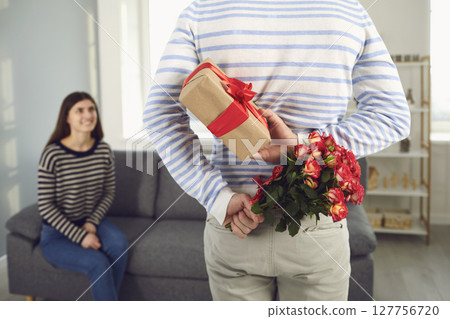 Valentine's day. Rear view of a man holding flowers and gives a girl a gift in his hands Valentine's day. Rear view of a man holding flowers and gives a girl a gift in his hands 127756720