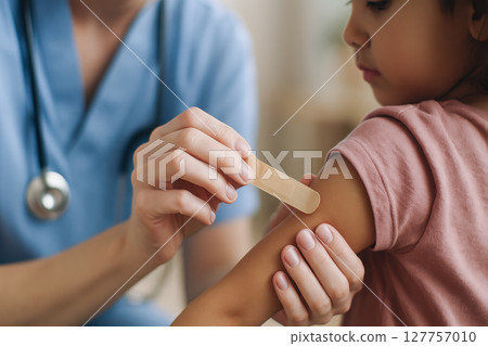 Healthcare professional gently applies bandage on child arm after vaccine, showing care and comfort during vaccination process to ensure child well being 127757010