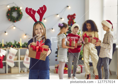 Girl holds out a Christmas present in front of her in a room with Christmas decorations. Girl holds out a Christmas present in front of her in a room with Christmas decorations. 127757014