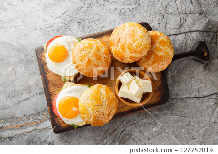 Delicious breakfast sandwiches with fried egg, butter, tomatoes, cheese, lettuce close-up on wooden board on table. horizontal top view Delicious breakfast sandwiches with fried egg, butter, tomatoes, cheese, lettuce close-up on wooden board on table. horizontal top view 127757019