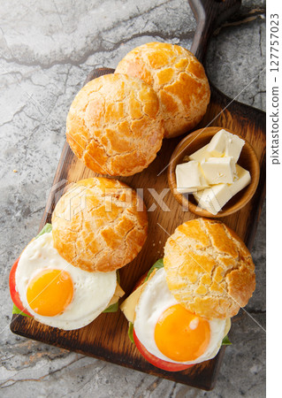 Chinese pineapple bun sandwich with fried egg, butter, tomato, cheese, lettuce close-up on wooden board. Vertical top view 127757023