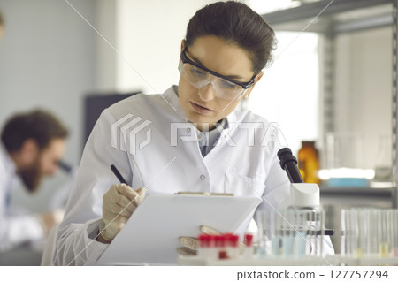 Scientist taking notes while doing medical research in modern science laboratory Scientist taking notes while doing medical research in modern science laboratory 127757294