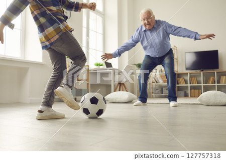 Little kid and his grandpa playing soccer at home and having fun together together 127757318
