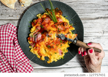 Woman eating polenta with sausage, tomato sauce and chives on rustic wooden table 127757431
