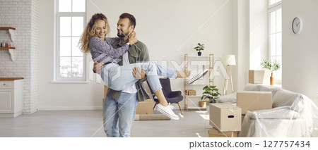 Happy loving husband holding his beloved wife in his arms in their new house during move. 127757434