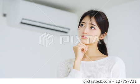 The expression of a young woman who is worried about whether to repair or replace her broken air conditioner The expression of a young woman who is worried about whether to repair or replace her broken air conditioner 127757721