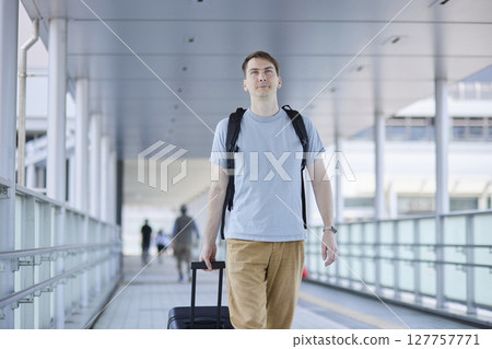 Male traveler walking through airport with suitcase and backpack 127757771