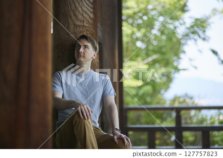一位男遊客坐在古老寺廟的陽台上,欣賞自然風光。 一位男遊客坐在古老寺廟的陽台上,欣賞自然風光。 127757823