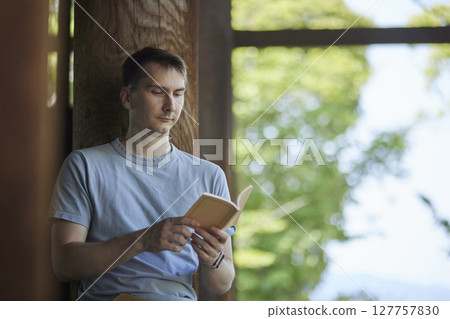 一個背著背包的男人在鬱鬱蔥蔥的古老寺廟的走廊上看書。 一個背著背包的男人在鬱鬱蔥蔥的古老寺廟的走廊上看書。 127757830