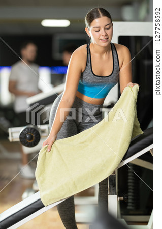 Girl puts towel on simulator and prepares equipment for training. 127758592