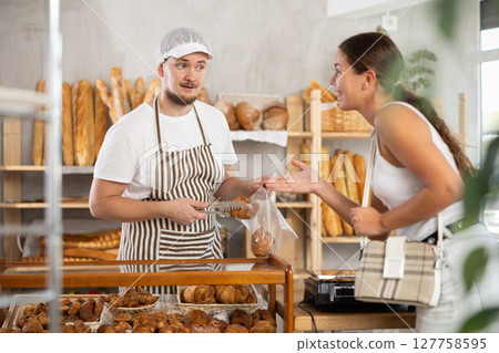 Salesman gives croissants to young girl in bakery 127758595