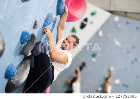Man climbing a tall, indoor, man made rock climbing wall Man climbing a tall, indoor, man made rock climbing wall 127758596