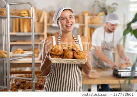 Female seller holds basket with finished products, shows many croissants 127758601