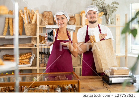 Saleswoman displays phone app standing next to salesman with baguettes 127758625