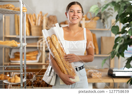 Positive young girl holding baguettes in plastic bag in bakery Positive young girl holding baguettes in plastic bag in bakery 127758639