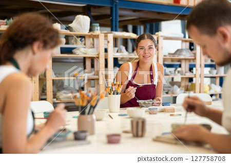 Pottery workers paint ceramic plates together at table Pottery workers paint ceramic plates together at table 127758708