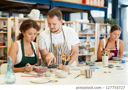 During master class, student paints clay vessel under guidance of male teacher. During master class, student paints clay vessel under guidance of male teacher. 127758727
