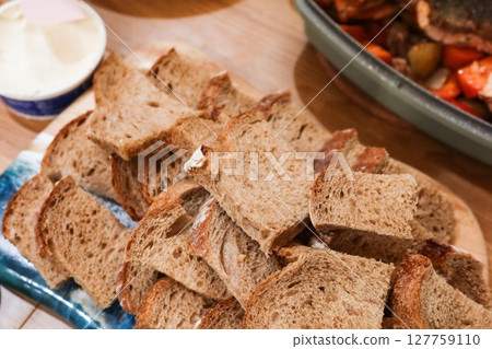 close up of a neatly arranged stack of sliced brown bread, likely whole grain or rye, displayed on a wooden board, with butter on the side close up of a neatly arranged stack of sliced brown bread, likely whole grain or rye, displayed on a wooden board, with butter on the side 127759110