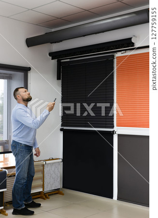 Man Demonstrating Automated Blinds in Sun Protection Showroom 127759155