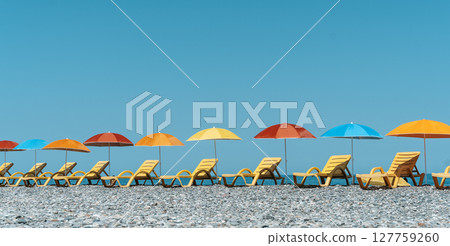 Colorful Beach Umbrellas and Sun Loungers on a Pebble Seaside Colorful Beach Umbrellas and Sun Loungers on a Pebble Seaside 127759260