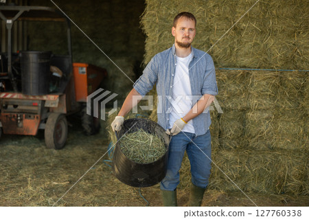 Young man with bucket of hay in barn 127760338