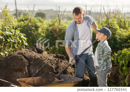 Young man and boy putting soil in wheelbarrow Young man and boy putting soil in wheelbarrow 127760341