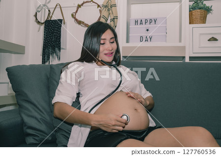 Pregnant woman enjoying an intimate moment listening to her baby's heartbeat at home, showcasing maternal affection. Pregnant woman enjoying an intimate moment listening to her baby's heartbeat at home, showcasing maternal affection. 127760536