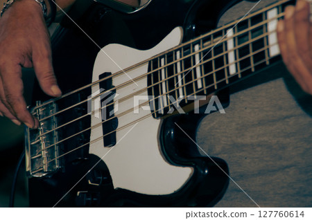 A close-up of hands playing a bass guitar, showcasing the instrument's unique design and vibrant details. 127760614